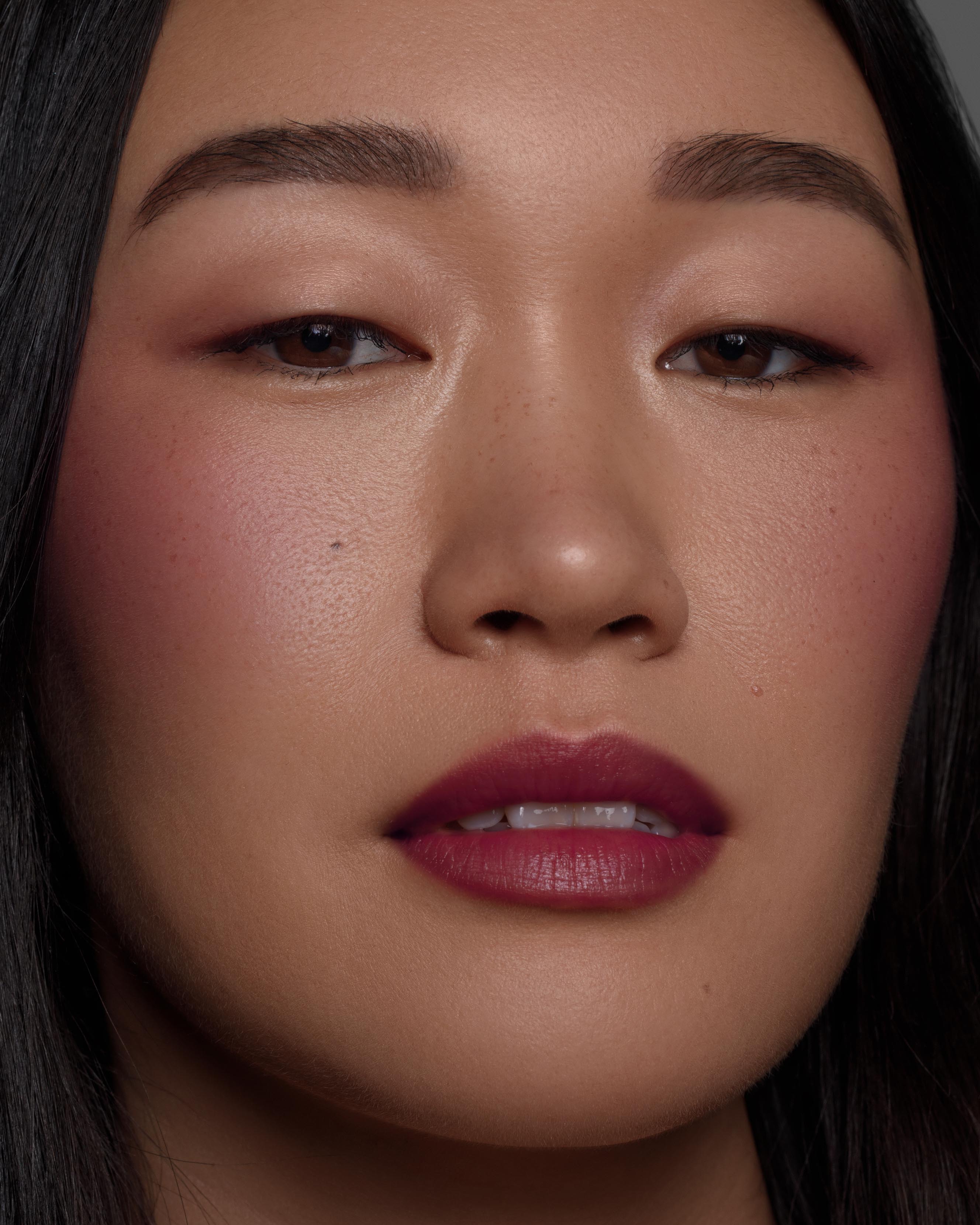 Close-up of a model with medium skin wearing purple makeup on lips, eyes, and cheeks